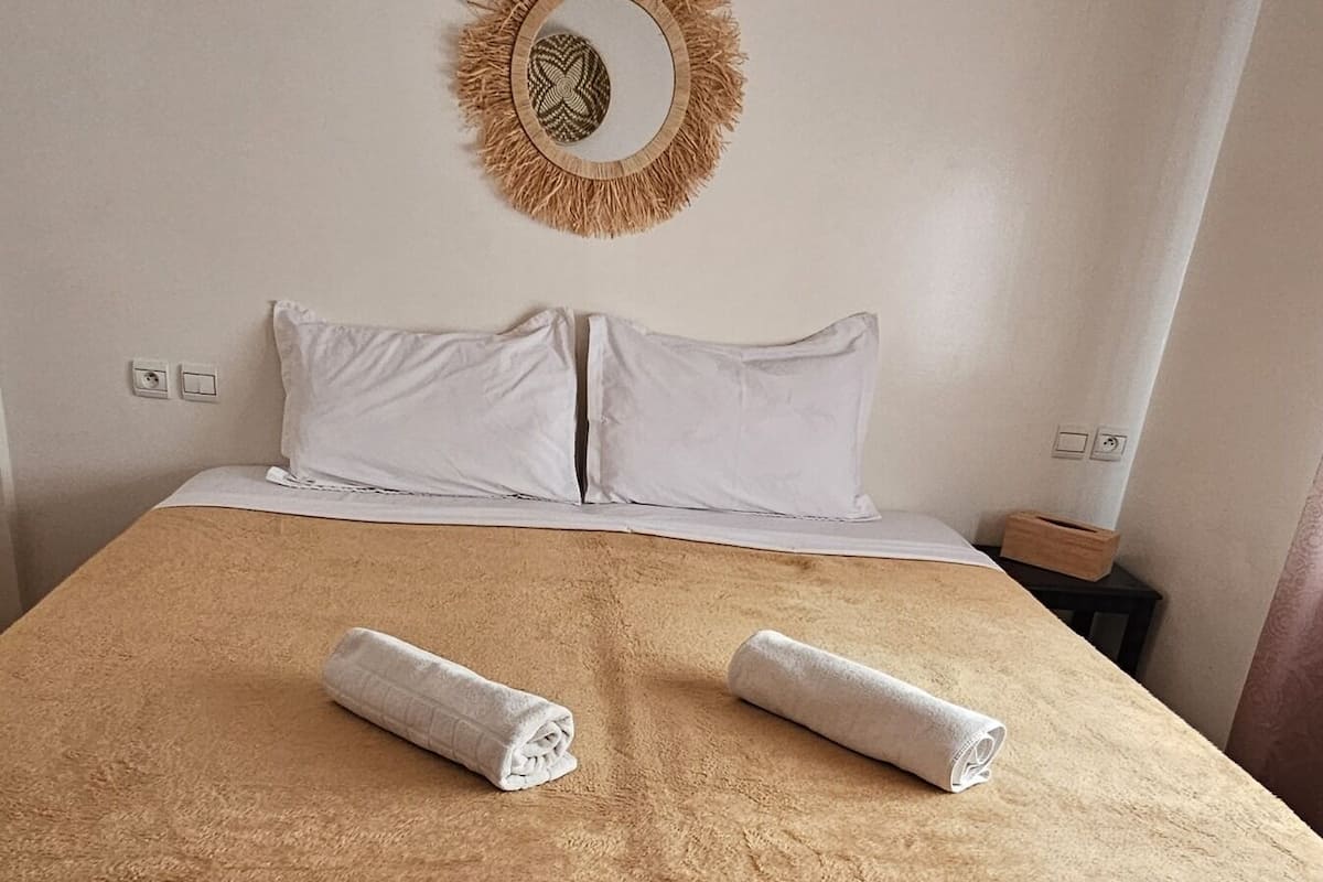 A neatly made bed with a brown cover, white pillows, and two rolled towels.