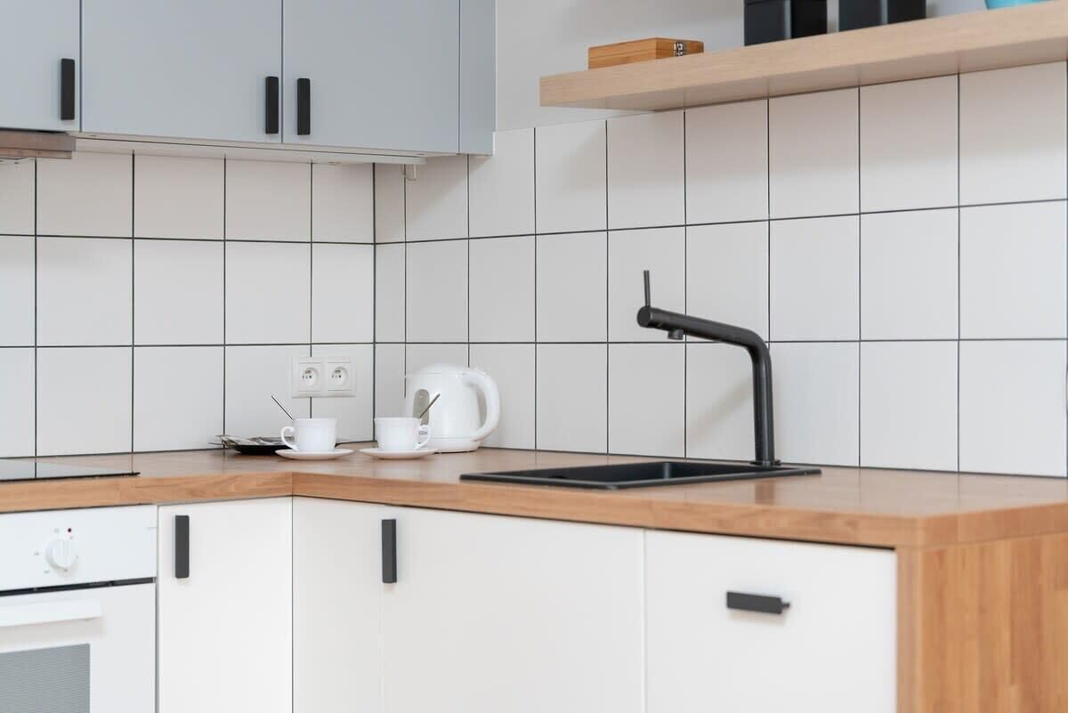 Una cucina moderna con mobili bianchi, un piano di lavoro in legno, un rubinetto nero e un bollitore.