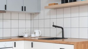Una cocina moderna con armarios blancos, encimera de madera, grifo negro y hervidor.