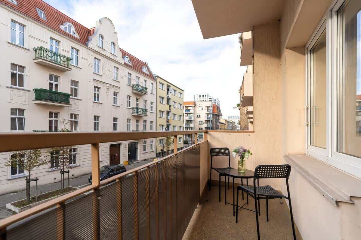 Un balcone con tavolo e sedie, affaccia su una strada con edifici.