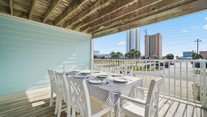 A covered outdoor dining area with a table set for four, white chairs, and a view of the cityscape.