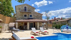 A stone villa with a swimming pool, outdoor seating, and a covered patio.