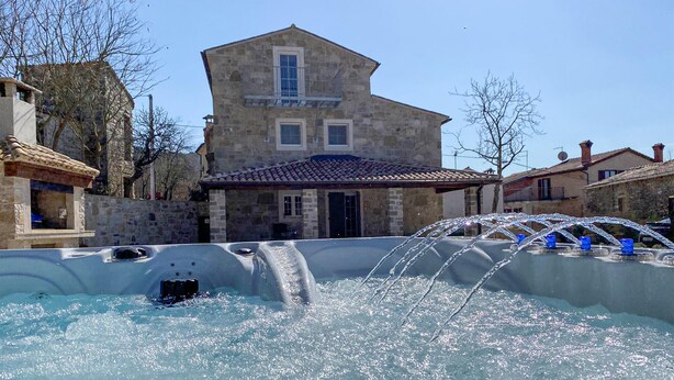 A stone building with a tiled roof, a hot tub with water jets, and a clear blue sky.