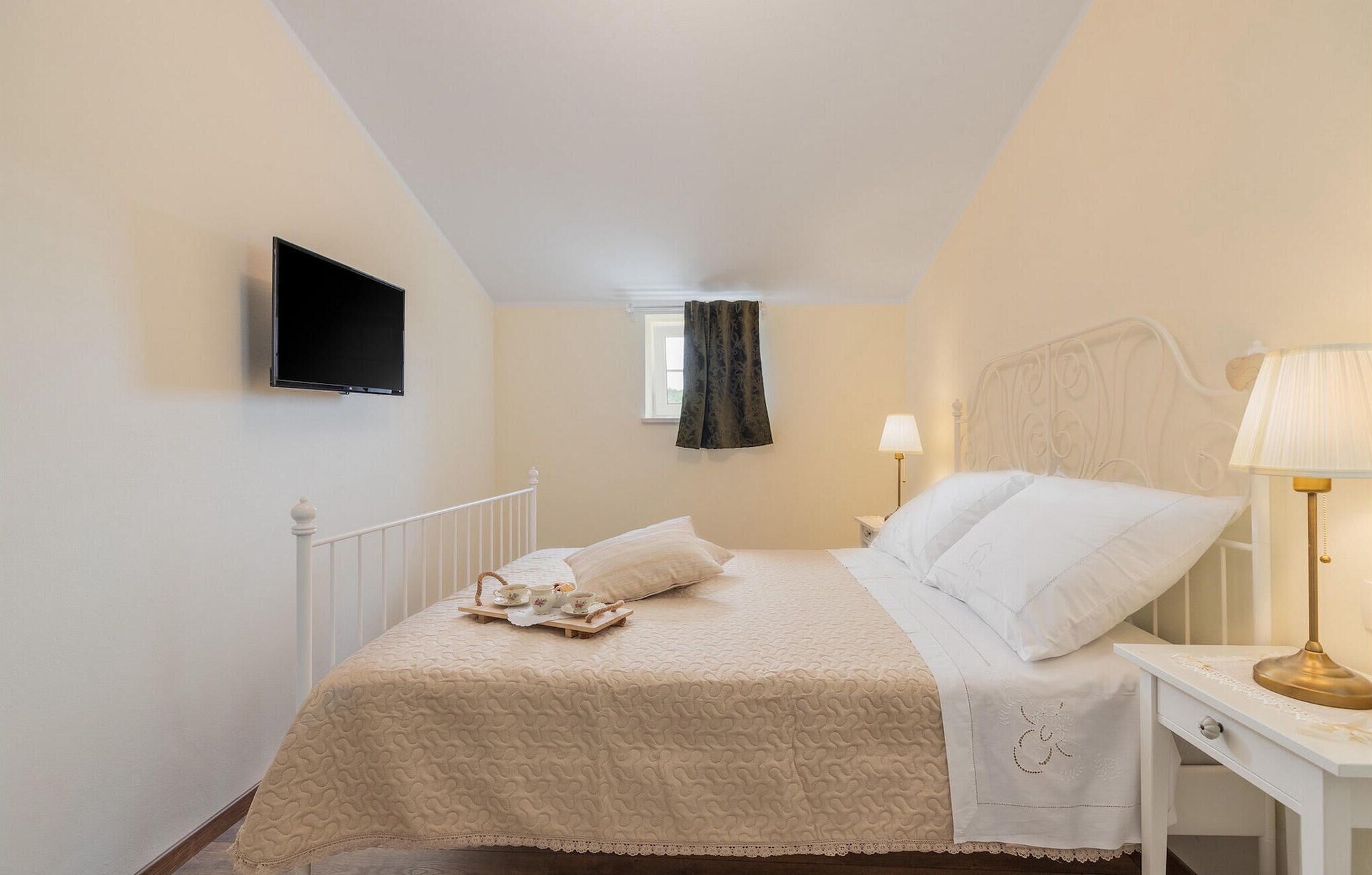 A bedroom with a bed, bedside table, lamp, and a TV mounted on the wall.