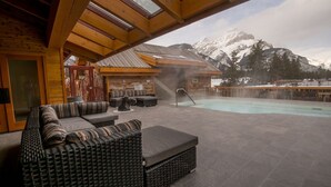 Een wellnessruimte met een jacuzzi, zitplaatsen en uitzicht op besneeuwde bergen.