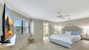 A bedroom with a bed, a ceiling fan, a TV, and a window with blinds. - Valencia in Pelican Bay (Naples)
