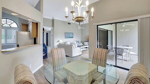 A spacious living area with a glass dining table, striped chairs, a chandelier, and a view to a balcony. - Valencia in Pelican Bay (Naples)
