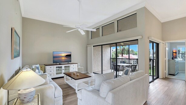 A spacious living room with a sofa, coffee table, TV, and a balcony with outdoor seating. - Valencia in Pelican Bay (Naples)