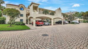 A multi-story hotel with a covered parking area and a paved driveway. - Valencia in Pelican Bay (Naples)