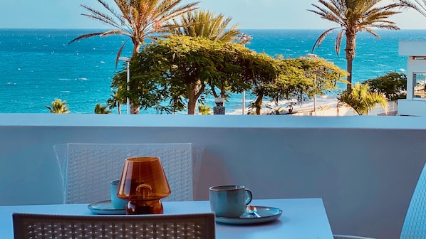 Ein Tisch mit Lampe und zwei Tassen mit Blick auf einen Strand, an dem Palmen und das Meer zu sehen sind.