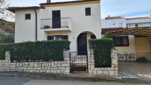 Un edificio de dos pisos con un muro de piedra, un portón negro y un pequeño balcón con plantas.