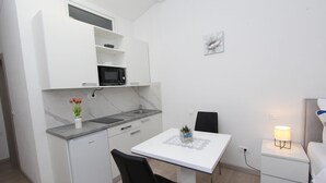 Cocina compacta con muebles blancos, microondas y un pequeño comedor con mesa y sillas.