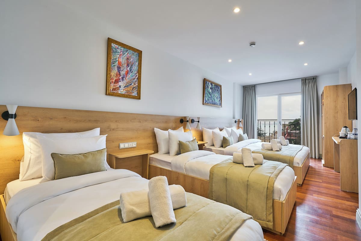 A hotel room with three beds, wooden headboards, and a large window with curtains.