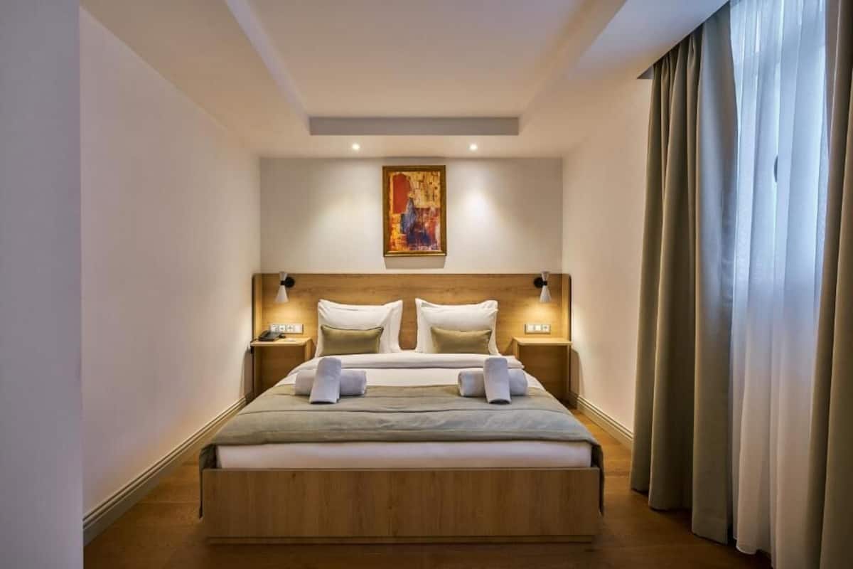A modern hotel room with a large bed, wooden headboard, bedside lamps, and a painting on the wall.
