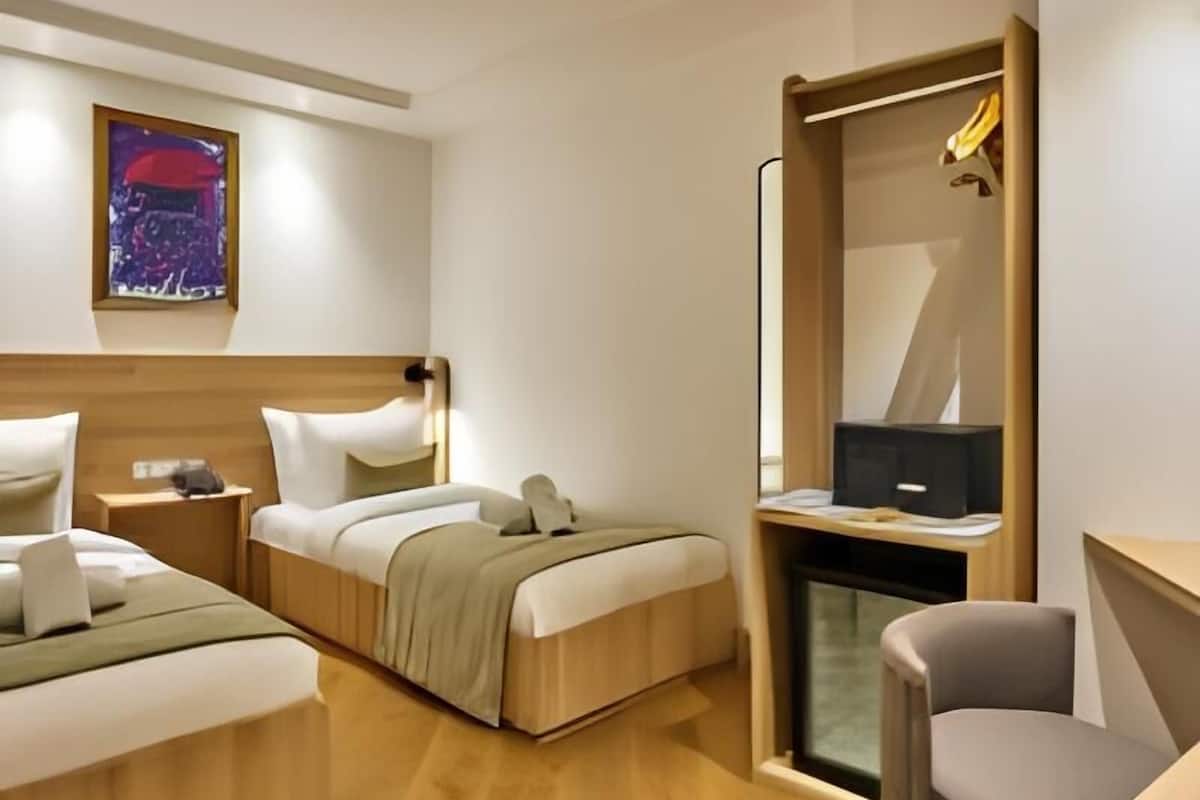 A hotel room with two beds, a desk, a chair, a mirror, and a painting on the wall.