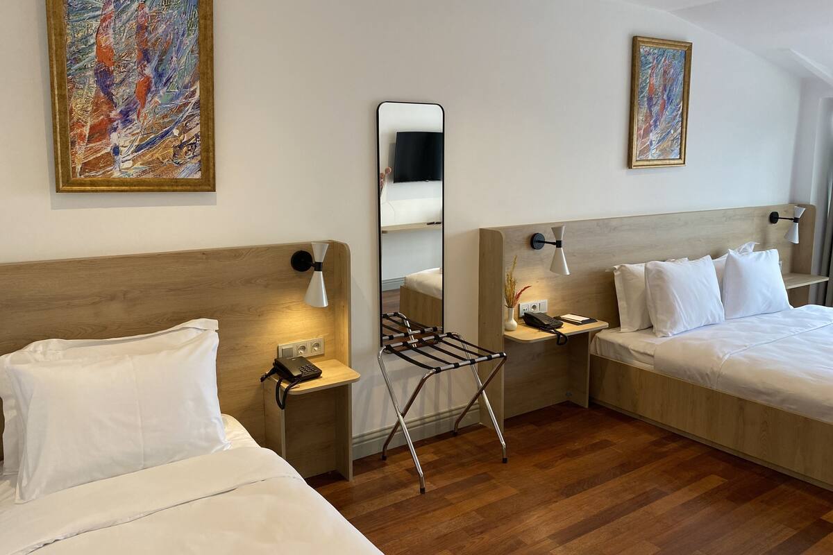A hotel room with two beds, a wooden headboard, a mirror, a bedside table with a lamp, a phone, and a small plant.