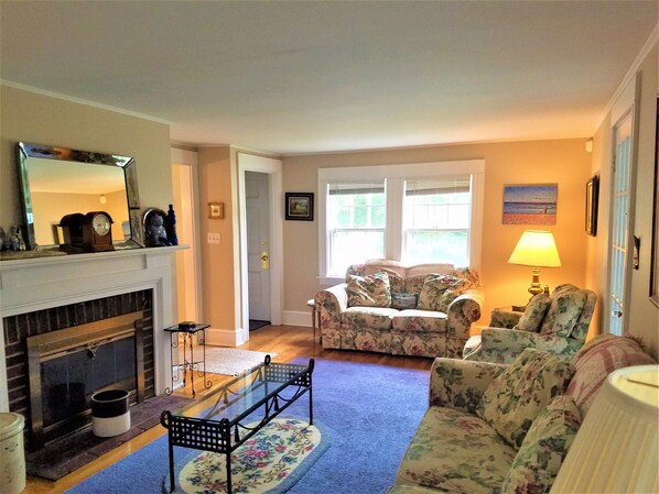 A living room with a fireplace, floral sofa, and a glass coffee table. - Short Distance to Colonial Acres Beach (2342) (West Yarmouth)
