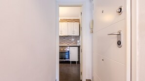 Un pasillo estrecho que conduce a una cocina con armarios blancos, salpicadero de azulejos y electrodomésticos de acero inoxidable.