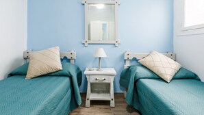 Una habitación con dos camas, cada una con ropa de cama color turquesa y almohadas a juego, una mesita de noche pequeña con una lámpara y un espejo en la pared.
