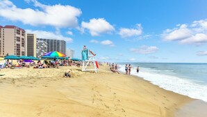 Una playa con sombrillas, una torre de salvavidas y edificios al fondo.
