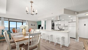 Una cocina moderna con armarios blancos, una isla central y un comedor con mesa y sillas de madera.