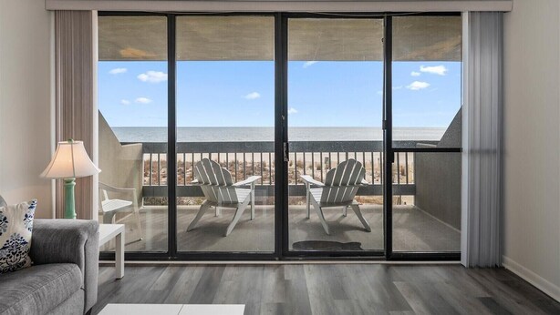 A room with a large sliding glass door leading to a balcony with two Adirondack chairs and a view of the beach. - Century I Condo with Ocean Views & Outdoor Pool! (Ocean City)