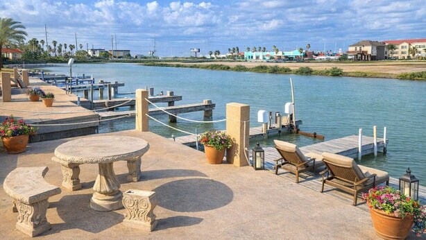A waterfront patio with a table, chairs, and potted plants. - Bay Sunset Views - Waterfront Pool - Boat Slip (Port Isabel)