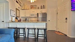 A modern kitchen with white cabinets, a microwave, and a stainless steel refrigerator. There are four bar stools in front of the kitchen island. - Bay Sunset Views - Waterfront Pool - Boat Slip (Port Isabel)