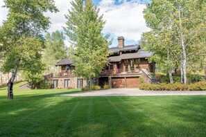A two-story log cabin with a stone chimney, a covered porch, and a garage. - Canyon Run Home - Upscale 5BR Ketchum Home with Yard and Sauna (Ketchum)