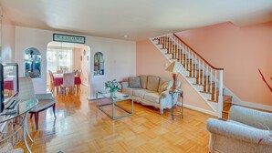 A spacious living room with a wooden staircase, a sofa, a coffee table, and a dining area with chairs and a table. - Quaint Lansdowne Getaway Near Downtown Philly! (Lansdowne)