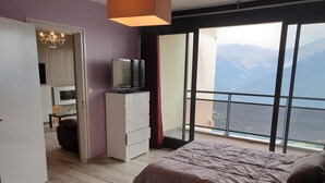 Een slaapkamer met een groot bed, een televisie op een dressoir en een balkon met uitzicht op de bergen.