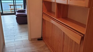 Een houten kast met meerdere lades en planken, een houten vloer en uitzicht op een balkon met een bankje.