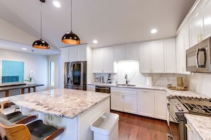 Uma cozinha moderna com armários brancos, bancadas de granito, eletrodomésticos de aço inoxidável e iluminação pendente.