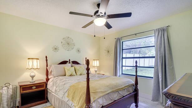 A bedroom with a four-poster bed, two bedside tables with lamps, a nightstand, a window with curtains, and a ceiling fan. - Orlando Home: 6 Mi to Universal! (Orlando)