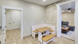 Een compacte leefruimte met een kitchenette, een eethoek met een houten tafel en banken, en een zithoek met een bank en salontafel.