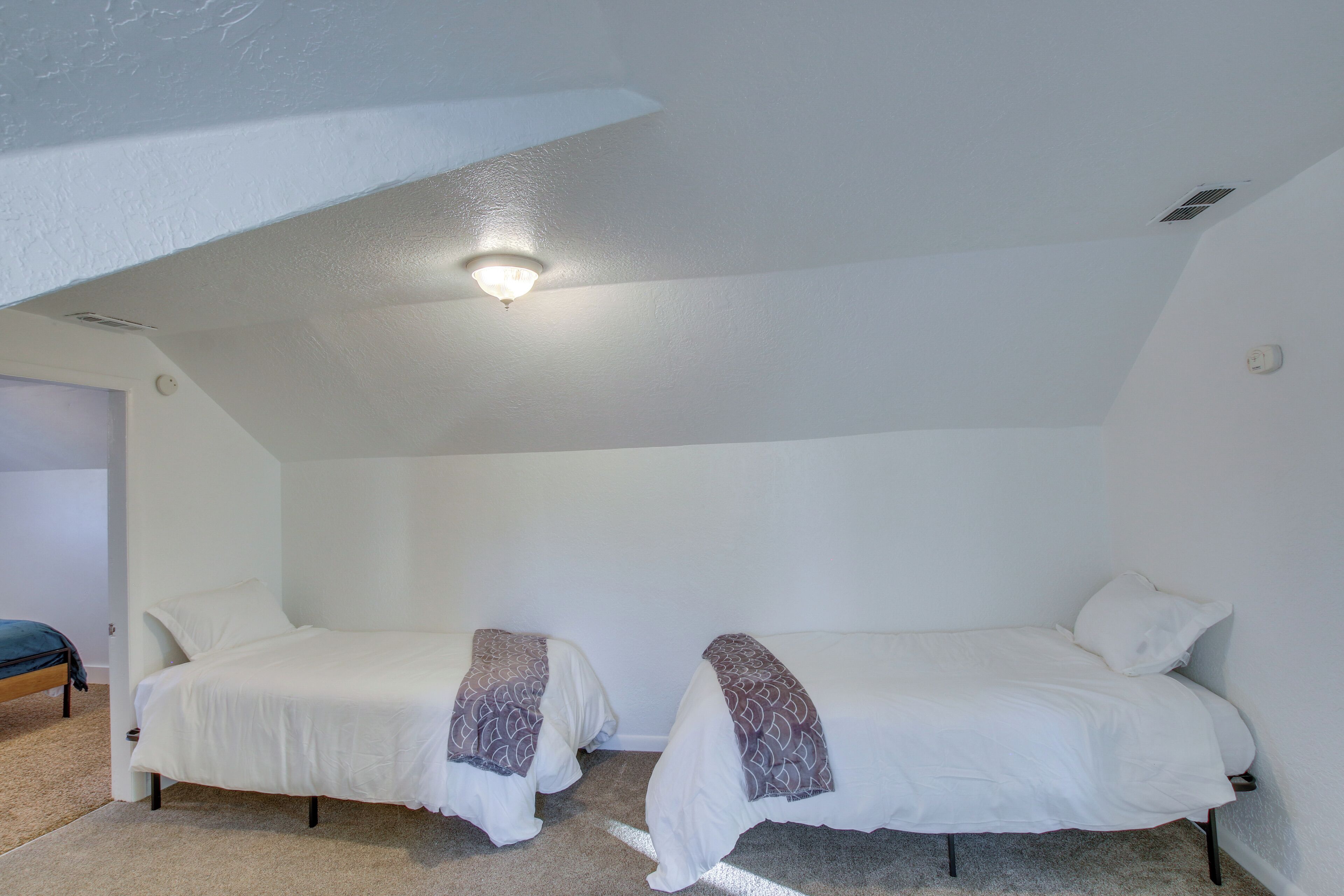 A small, white-walled room with two single beds, each with a patterned blanket.