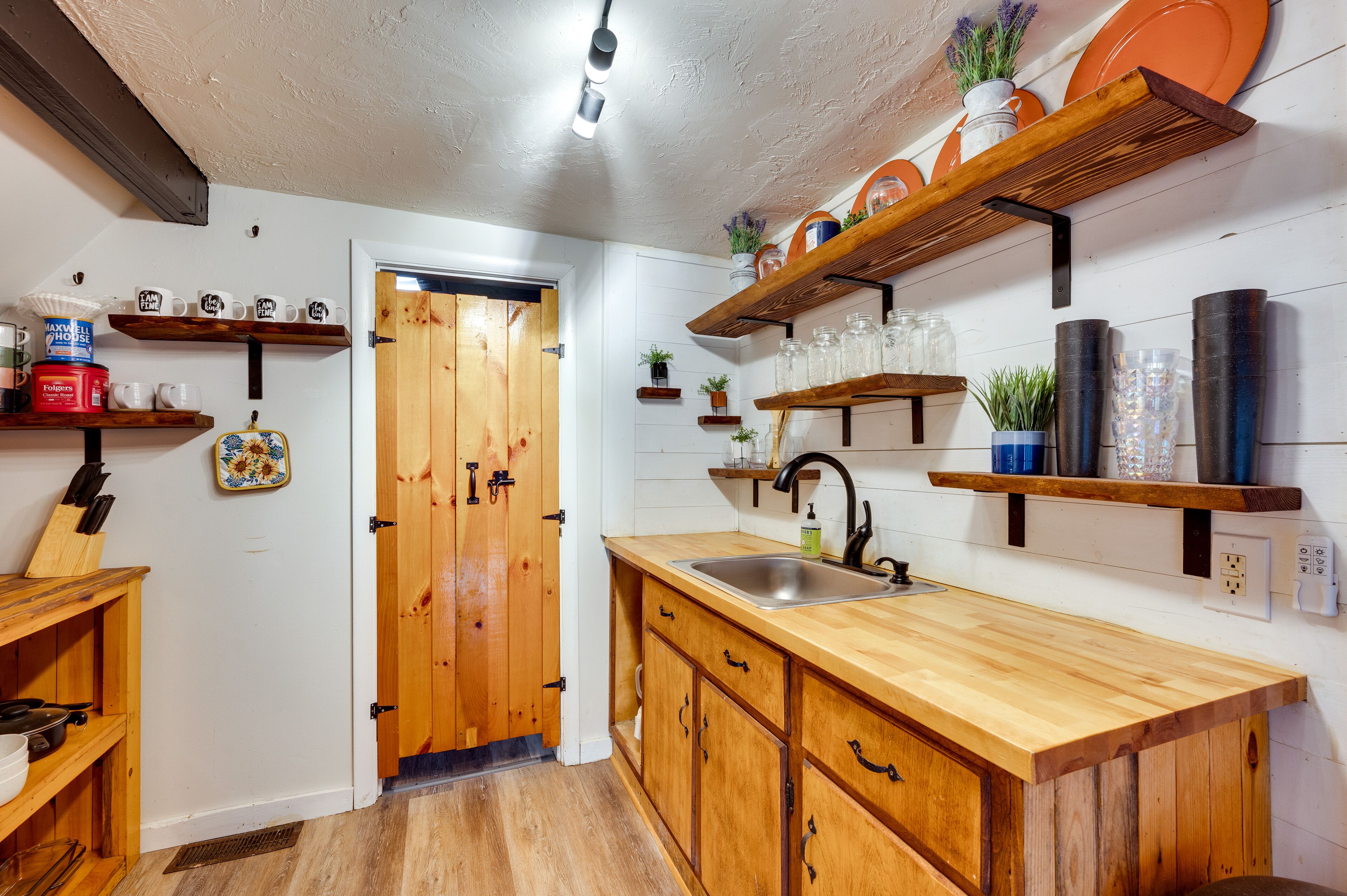 A kitchen with wooden cabinets, a sink, and shelves with various kitchen items.