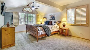 A bedroom with a sloped ceiling, a bed with a wooden frame, two bedside lamps, a wooden nightstand, a dresser, and a window with blinds.