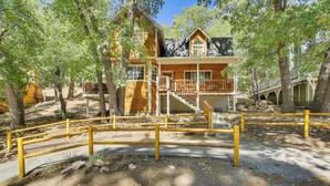 A log cabin with a wooden deck and a staircase leading to the upper level.