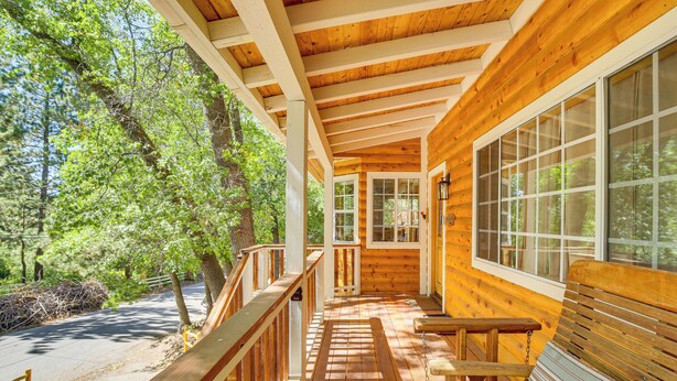 A wooden deck with a bench and railing, surrounded by trees.