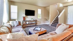 A living room with a sofa, ottoman, and a flat-screen TV mounted on the wall. - South Salt Lake Home w/ Hot Tub: 7 Mi to Downtown (Salt Lake City)