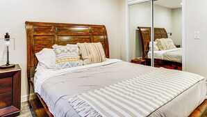 A neatly made bed with a wooden headboard, a bedside table with a lamp, and a large mirror on the wall. - South Salt Lake Home w/ Hot Tub: 7 Mi to Downtown (Salt Lake City)