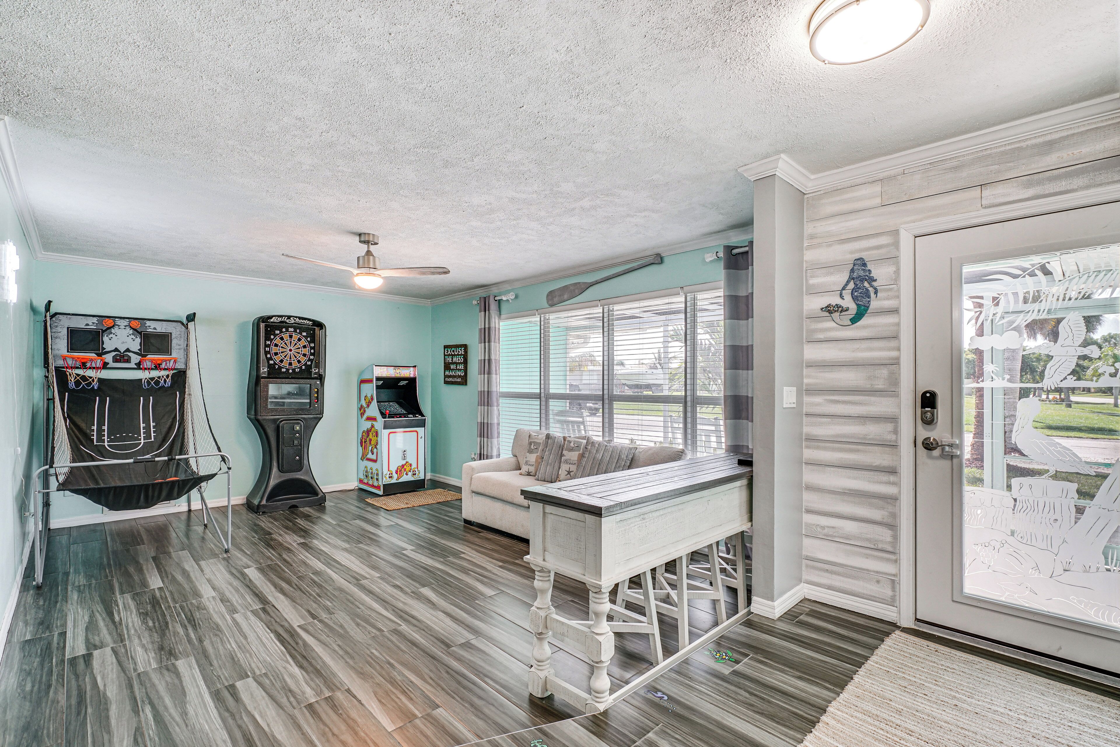 A room with a dartboard, a pool table, a sofa, and a door with a view of the outside.
