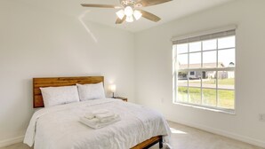A bedroom with a wooden bed, white bedding, a ceiling fan, and a large window with a view of the outside. - Airy Port Charlotte Home w/ Smart TV Near Beaches! (Port Charlotte)