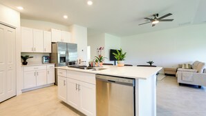 A modern kitchen with white cabinets, a dishwasher, and a countertop with a sink. There is a ceiling fan and a plant on the countertop. - Airy Port Charlotte Home w/ Smart TV Near Beaches! (Port Charlotte)