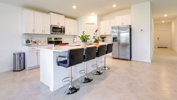 A modern kitchen with white cabinets, stainless steel appliances, and a central island with bar stools. - Airy Port Charlotte Home w/ Smart TV Near Beaches! (Port Charlotte)