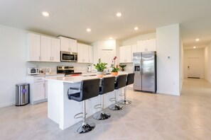 A modern kitchen with white cabinets, stainless steel appliances, and a central island with bar stools. - Airy Port Charlotte Home w/ Smart TV Near Beaches! (Port Charlotte)
