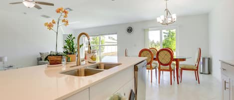 Une cuisine moderne dotée d’un grand îlot central, de deux éviers et d’un coin repas avec des chaises en bois.