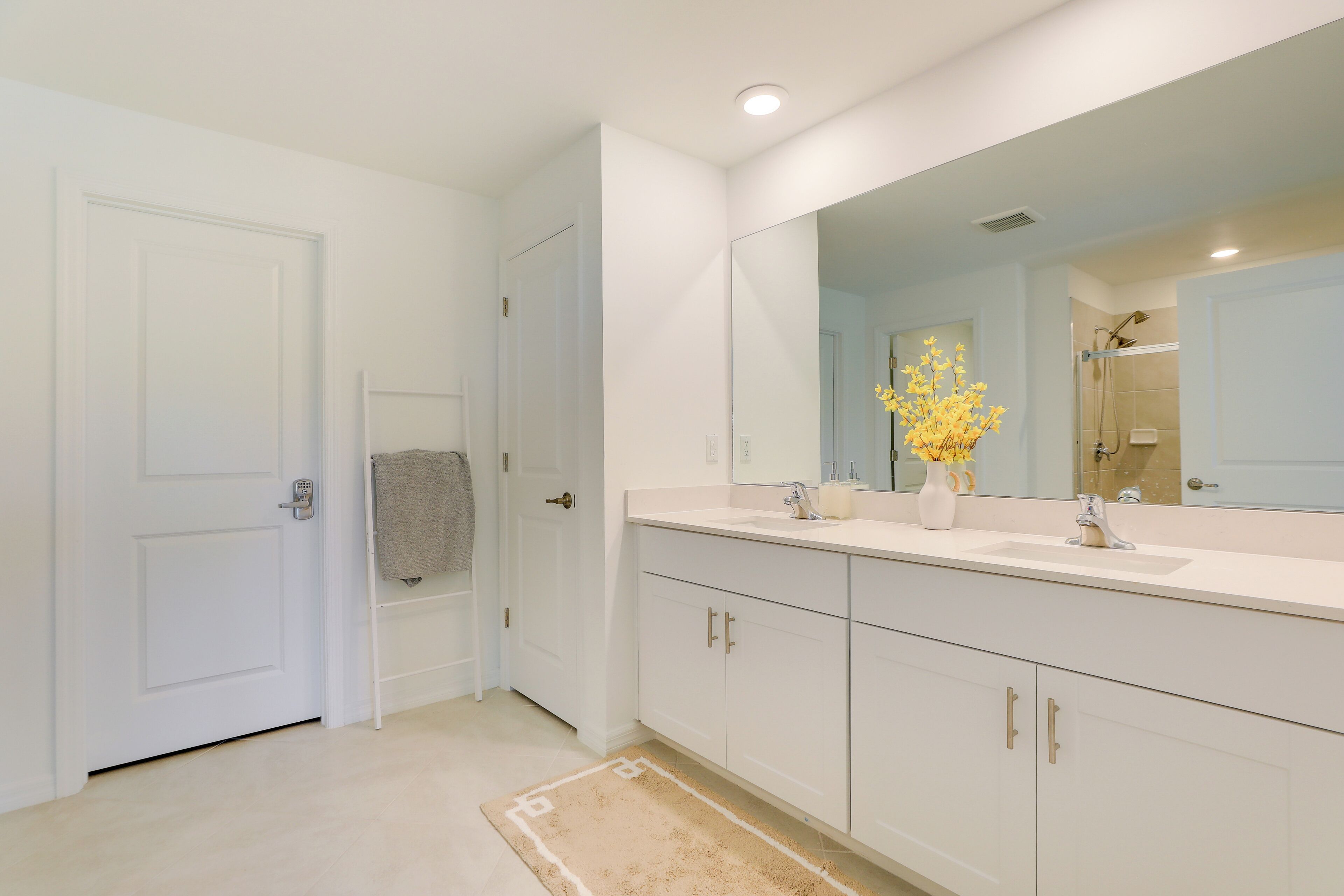 A modern bathroom with a large mirror, white cabinets, and a beige rug.