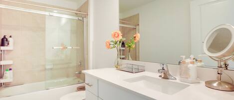 Un baño moderno con cabina de ducha de vidrio, un lavabo blanco con mueble y un espejo grande.